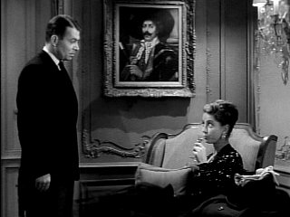 James Mason and Danielle Darrieux discuss plans. Some of their loot is hidden behind the painting, in a safe.